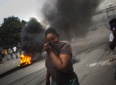 A woman covers her face from the smoke of burning tires set up by demonstrators in Port-au-Prince, who complain that UN peacekeepers are the source of the cholera epidemic sweeping the country.