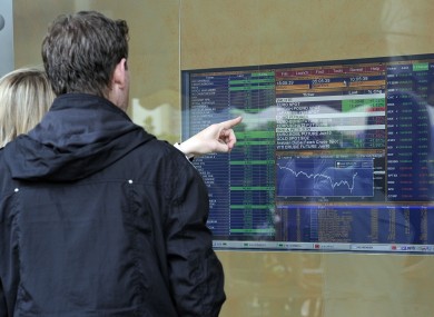 People check a monitor reporting financial data outside a bank in Milan.