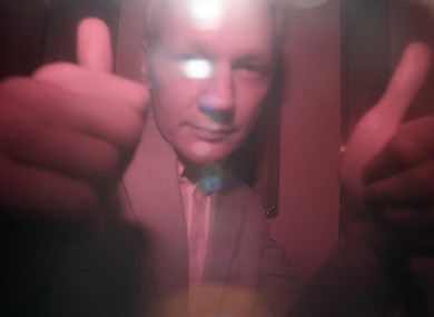 Julian Assange signals to photographers through the tinted window of a police van, following his appearance in court yesterday.