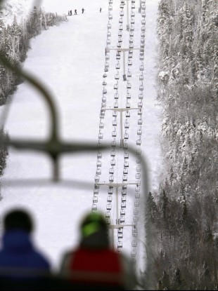 Skiers ride a chairlift with a view of Spillway East chair lift, background, where six people were injured when five chairs fell to the ground yesterday.