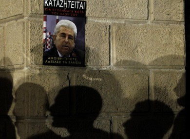 The silhouettes of protesters on a wall with a poster of Cyprus' president Dimitris Christofias that reads in Greek