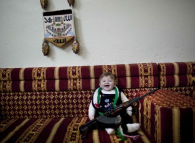 A six-month old poses with a machine gun owned by supporters of the Free Syrian Army. The photo was taken inside a house near Idlib in Syria.