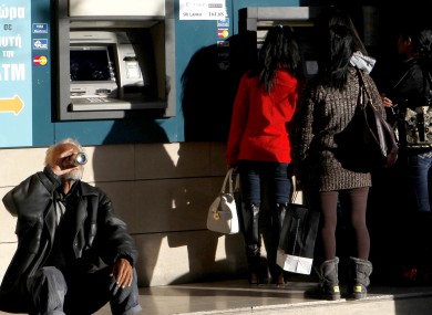 A man sits and drinks as women use the ATM outside of a Bank of Cyprus branch in Nicosia on Sunday