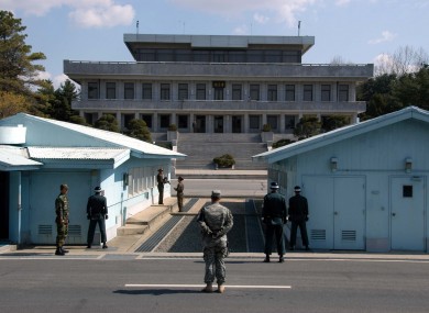 A US soldier stands on the South Korean side of the border between North and South Korea. South Korean soldiers are seen to the right; North Korean soldiers in the background.