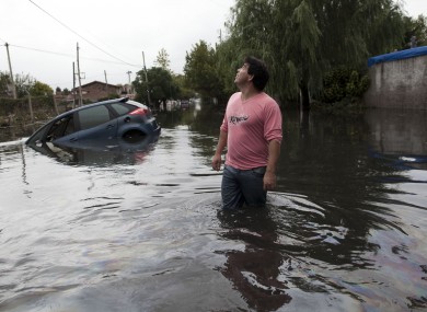 A man looks to the sky outside his home in a flooded street where a car is submerged in La Plata