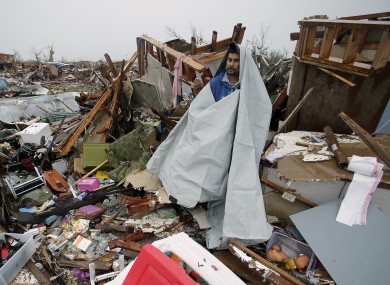 Victor Gonzalez seeks shelter from the rain under a sheet of plastic as he helps a friend salvage items from a tornado-ravaged home.