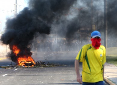 A masked protestor walks near a burning barricade as riot police stand guard near the Castelao stadium in Fortaleza, Brazil.