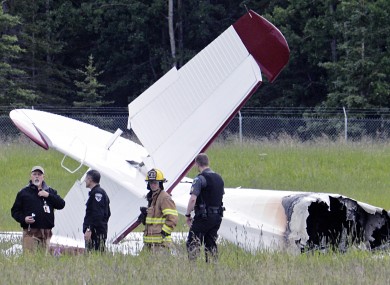 Police and emergency personnel stand near the remains of a fixed-wing aircraft that was engulfed in flames Sunday.