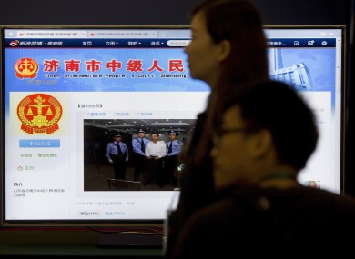 Journalists stand against a screen displaying a page from the Jinan Intermediate People's Court's website showing a photo of fallen politician Bo Xilai standing handcuffed as he is held by police at the court.