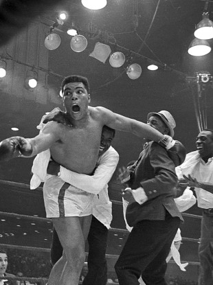 Cassius Clay's handlers hold him back as he reacts after he is announced the new heavyweight champion.