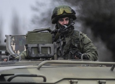 A man in unmarked uniform looks from atop of a military vehicle while standing guard as troops taking control the the Coast Guard offices in Balaklava
