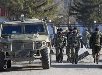 Ukrainian troops with white bands on their sleeves march past an unmarked Russian military vehicle outside a Ukrainian military base in Perevalne, Crimea.