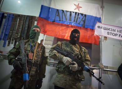 Masked pro-Russian gunmen guard an entrance of the Ukrainian regional office of the Security Service with a Russian National flag is in background in Luhansk, Ukraine.