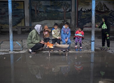 A Palestinian man sits with his children around fire to keep warm during a cold storm at a U.N. school where families live after their homes were destroyed by Israeli strikes in the summer, in Gaza City.