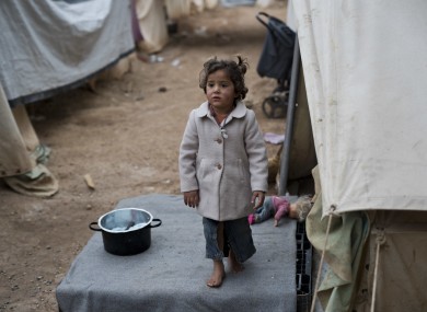 A child waits for her mother as she stands outside the family tent home at Ritsona refugee camp north of Athens.
