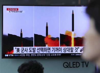 A woman walks by a TV news program showing images of North Korean missile launch, published in the country's Rodong Sinmun newspaper, at Seoul Railway station in Seoul.