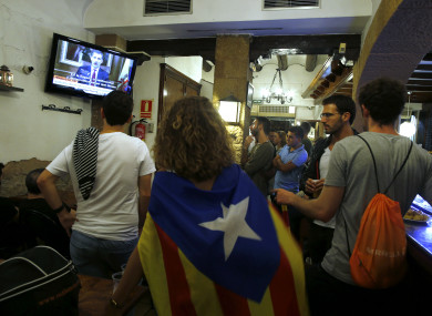 People, one of them with a Catalan independence flag around her shoulders, watch Spain's King Felipe's statement about the situation in Catalonia.