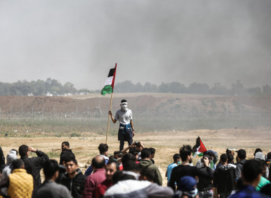 A Palestinian man holds his national flag as others burn tires to protect themselves from shots of Israeli soldiers at the Israel-Gaza border.