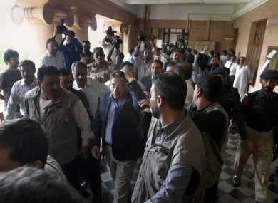 Pervez Musharraf, surrounded by guards, holds his head after a shoe was thrown at him outside a courtroom today