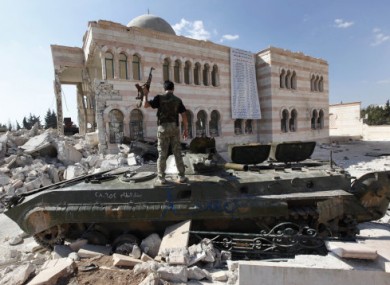 A Free Syrian Army soldier stands on a damaged Syrian military tank outside Aleppo