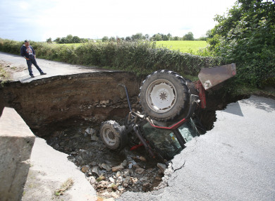 A man looks at a tractor which has fallen into a road collapsed in Iskaheen, County Donegal.