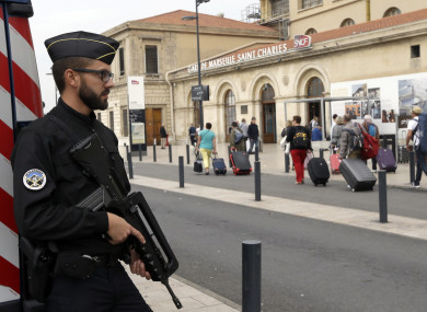 A police officer stands guard while passengers enter the Marseille Saint Charles train station, a day after a man fatally stabbed two women outside the train station.
