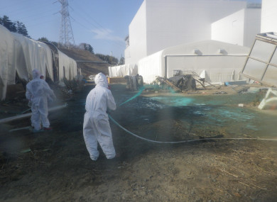 Workers wearing protective suits spray adhesive synthetic resin over the ground at the Tokyo Electric Power Co. (TEPCO)'s Fukushima Daiichi Nuclear Power Plant