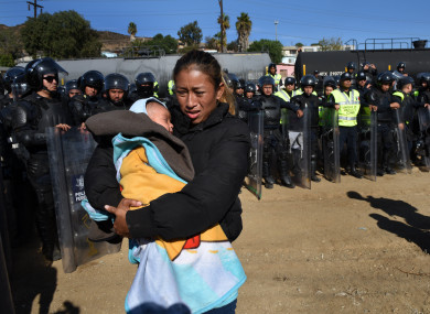 A woman and her 5 month-old baby walk past Mexican police in riot gear moving the migrants away from the border