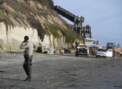 A San Diego County Sheriff's deputy looks on as search and rescue personnel work at the site of a cliff collapse at a popular beach.