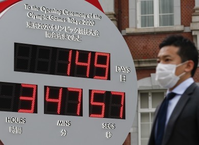 A man wearing a surgical mask walks past a big Omega One-Year Countdown clock for the opening ceremony of the Tokyo 2020 Olympic and Paralympic Games outside Tokyo Station.