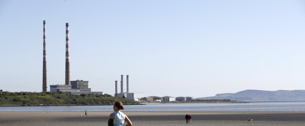 People enjoy sunny weather on Sandymount strand with by the Poolbeg chimney stacks in the background.