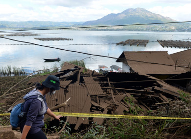 A woman walks past houses by Lake Batur which were damaged by an earthquake-triggered landslide in Bangli, on the island of Bali, Indonesia