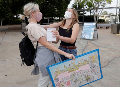 A woman, left, is embraced by a friend after arriving on a flight from Los Angeles at Sydney Airport