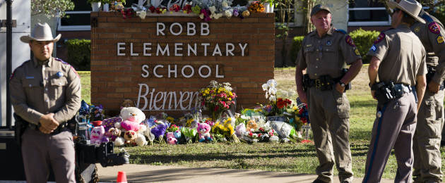 Officers guard the memorial by the entrance to Robb Elementary School in Uvalde